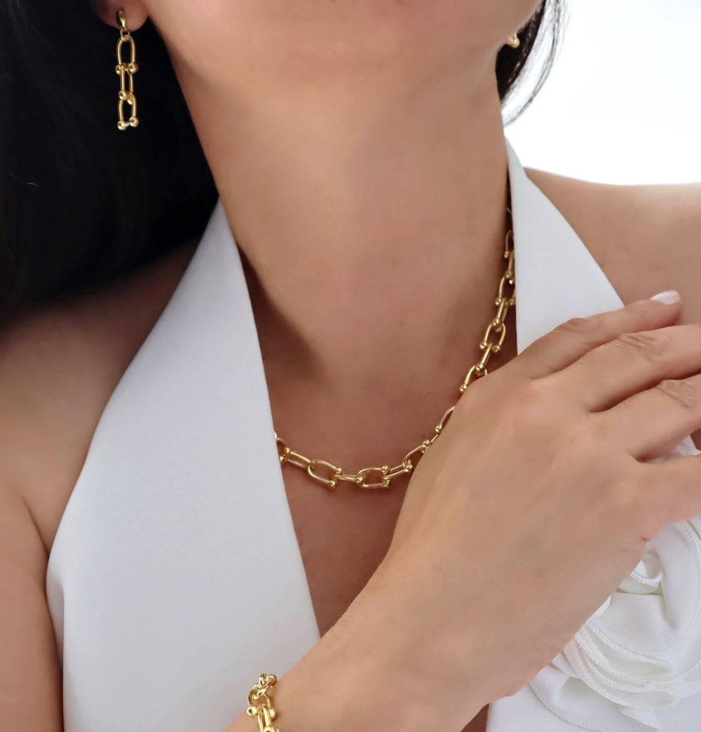 Gold gauge link chain earrings, necklace and bracelet on a person wearing a white top.