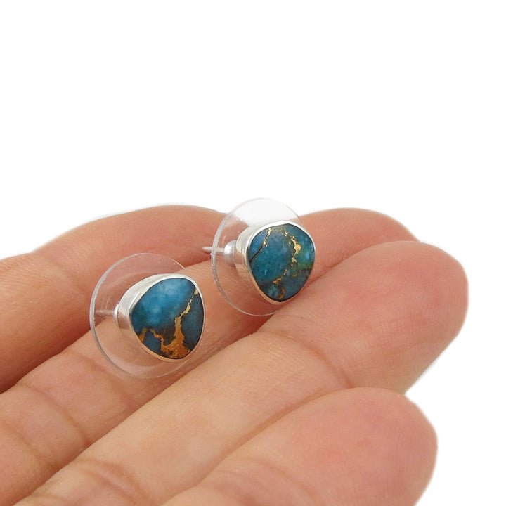 Turquoise and gold stud earrings held between fingers on a white background