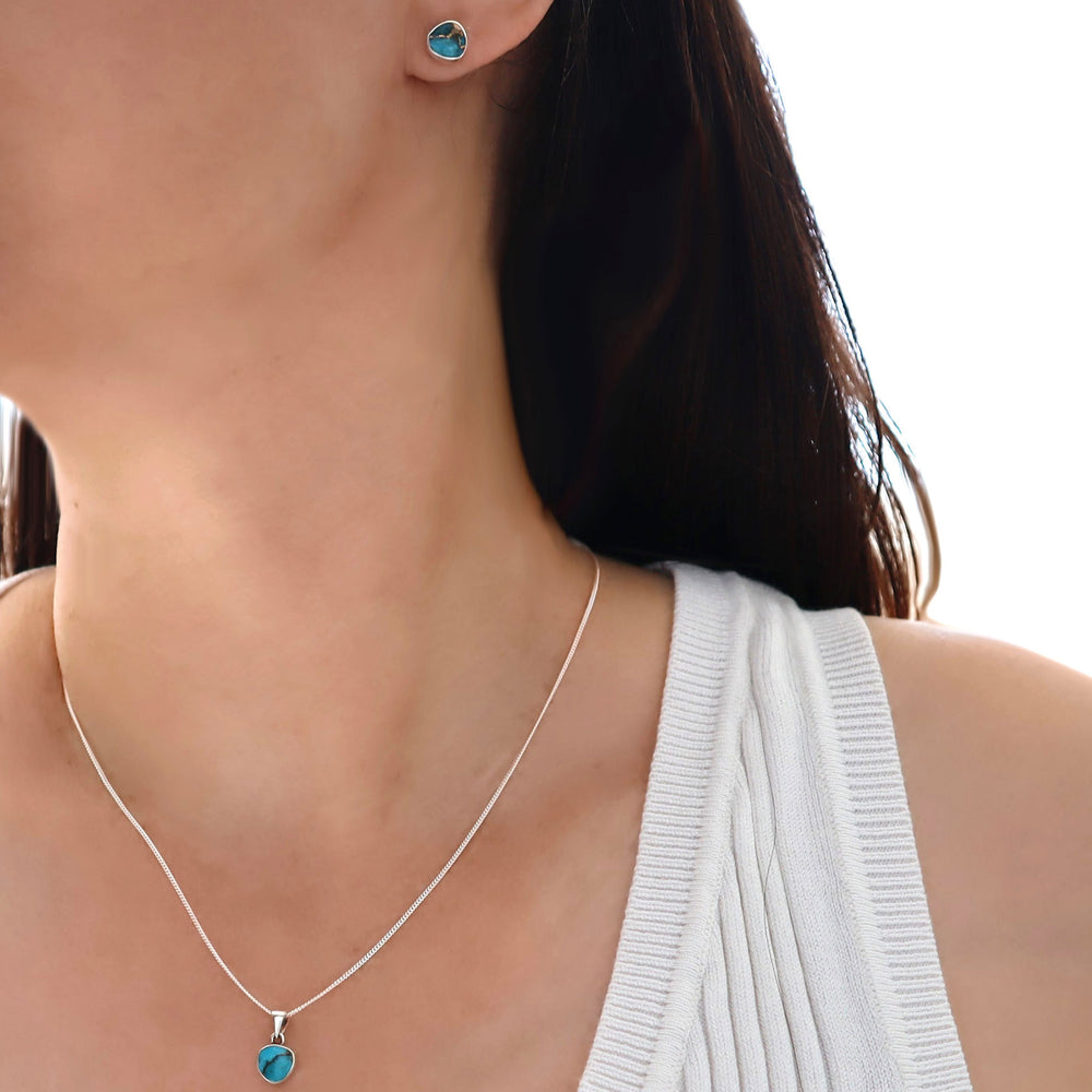 Close-up of a woman wearing a silver necklace with a turquoise blue pendant and matching turquoise earrings.