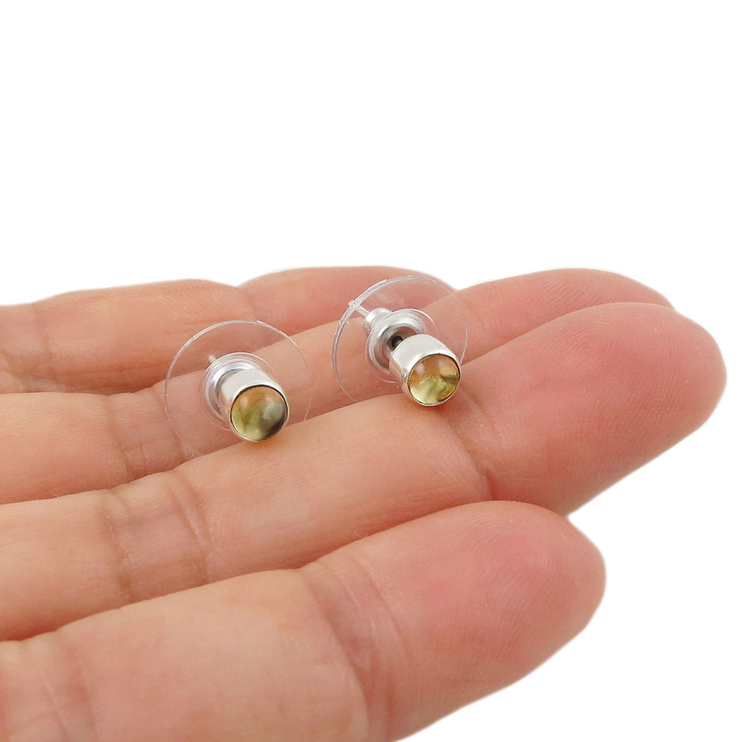 Small silver stud earrings with citrine  gemstones held between fingers on a white background