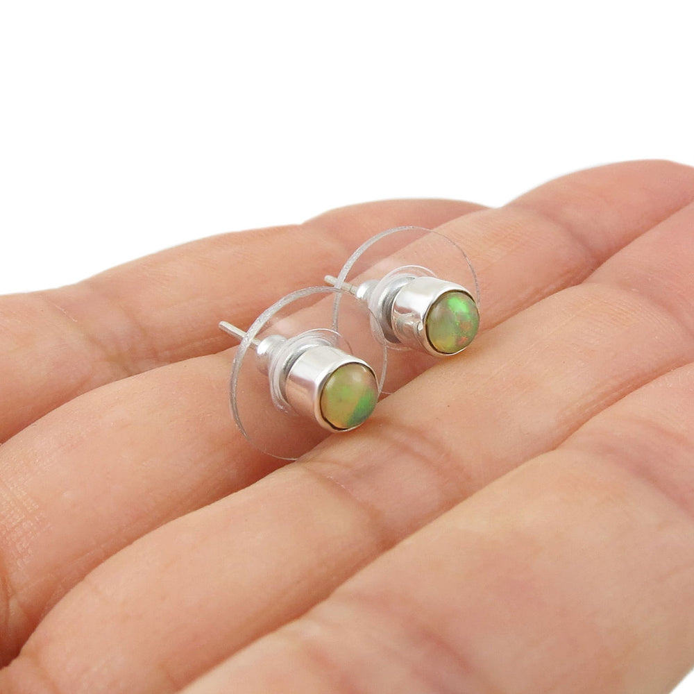 Pair of silver earrings with green opal gemstones held in a hand on a white background