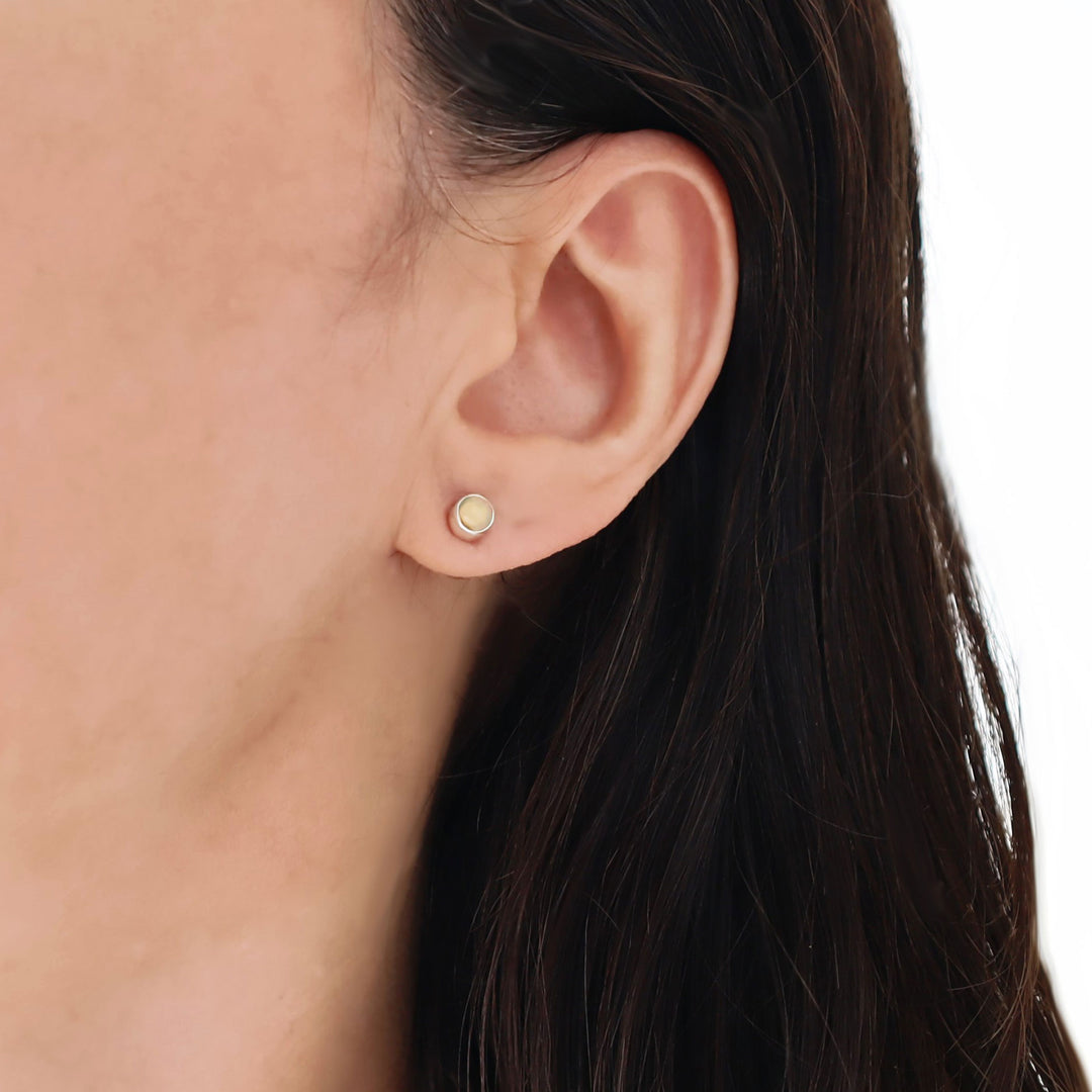 Close-up of an ear wearing a opal gemstone earring with a white background
