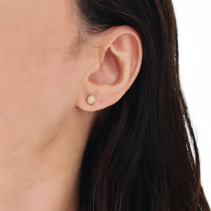 Close-up of an ear wearing a opal gemstone earring with a white background