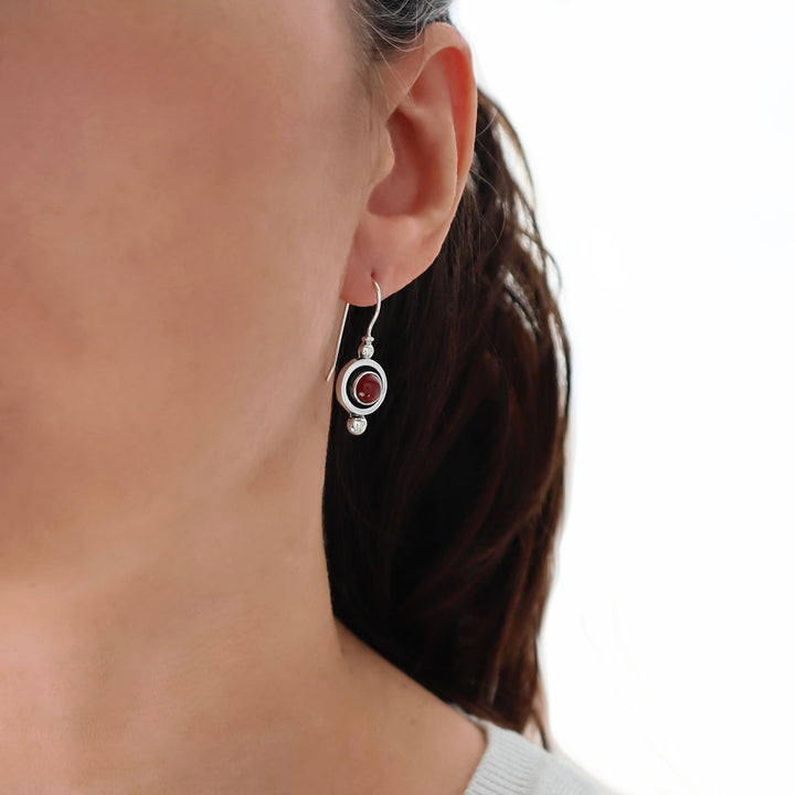 Close-up of a person wearing a silver earring with a red garnet gemstone on a neutral background