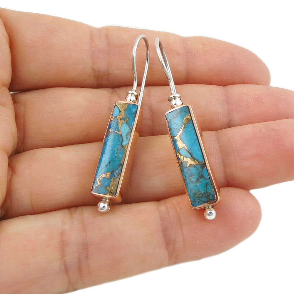 Turquoise stone earrings with gold accents held in a hand on a white background