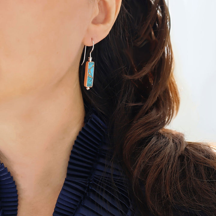 Turquoise gemstone earrings with copper and silver worn by a woman with long dark hair. 