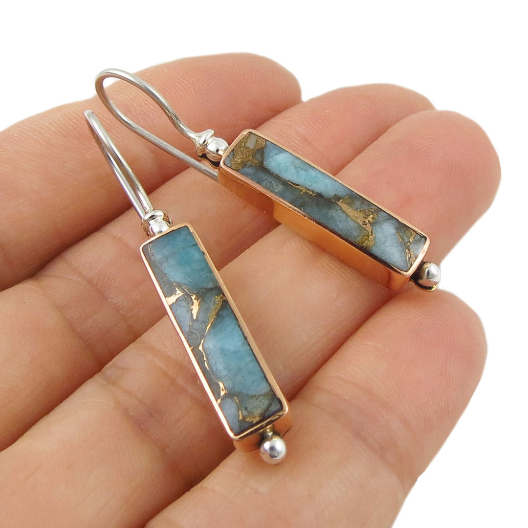 Blue amazonite gemstone earrings set in a copper base with silver ear hooks held in a person's hand.