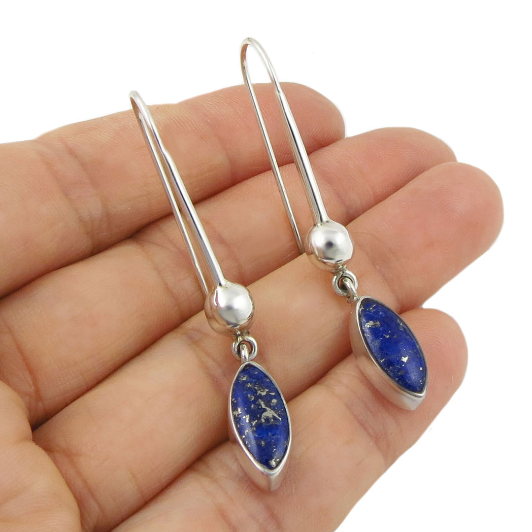 Long silver teardrop earrings with lapis lazuli gemstones held in a person's hand. 