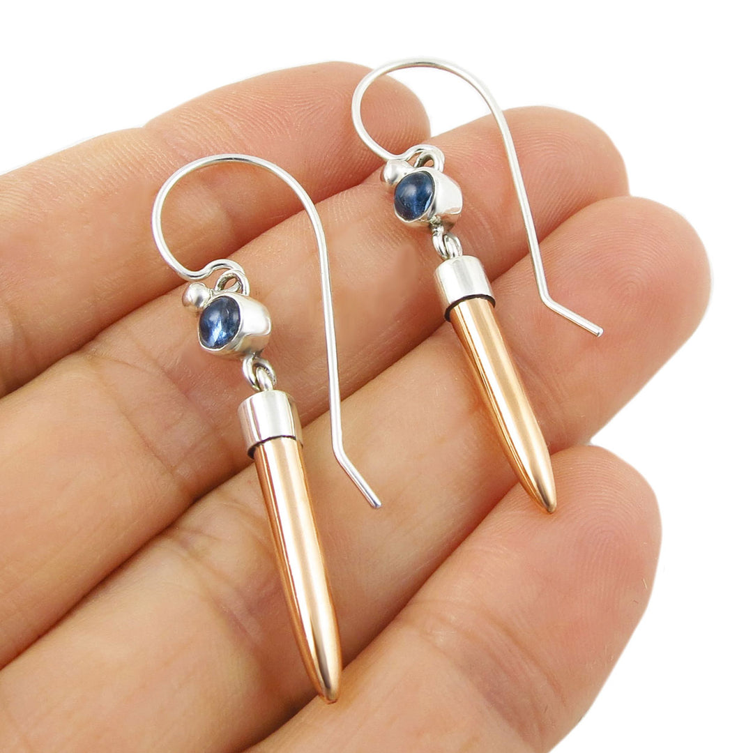 Blue topaz gemstones in mixed metal copper and 925 silver earrings held in a person's hand. 