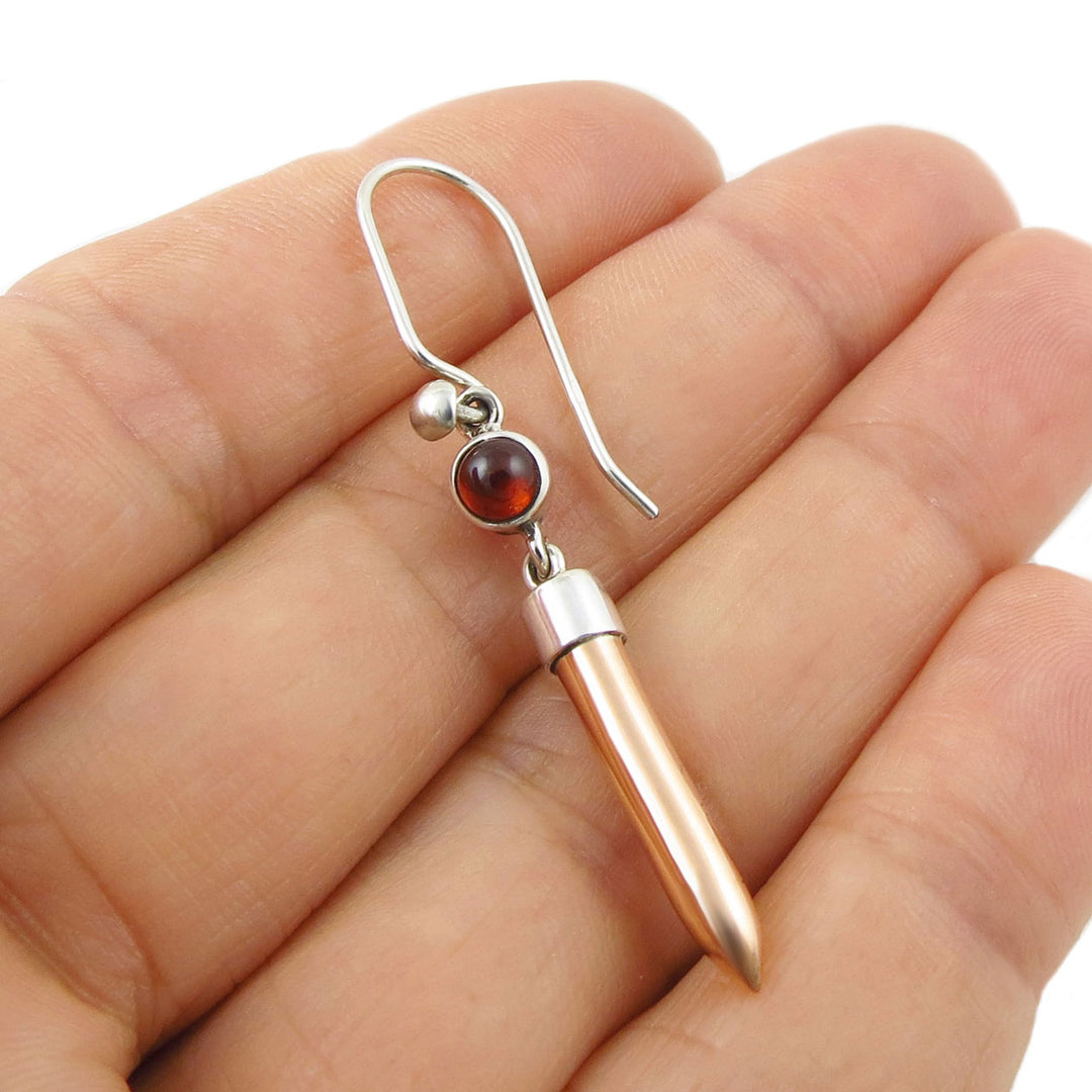 A single copper and silver earring with a red garnet gemstone held in a hand on a white background