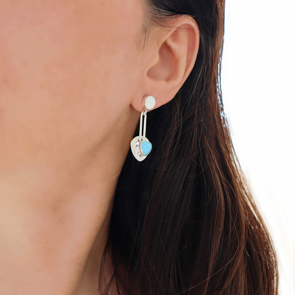 Close-up of a silver earring with a blue turquoise gemstone on a white background