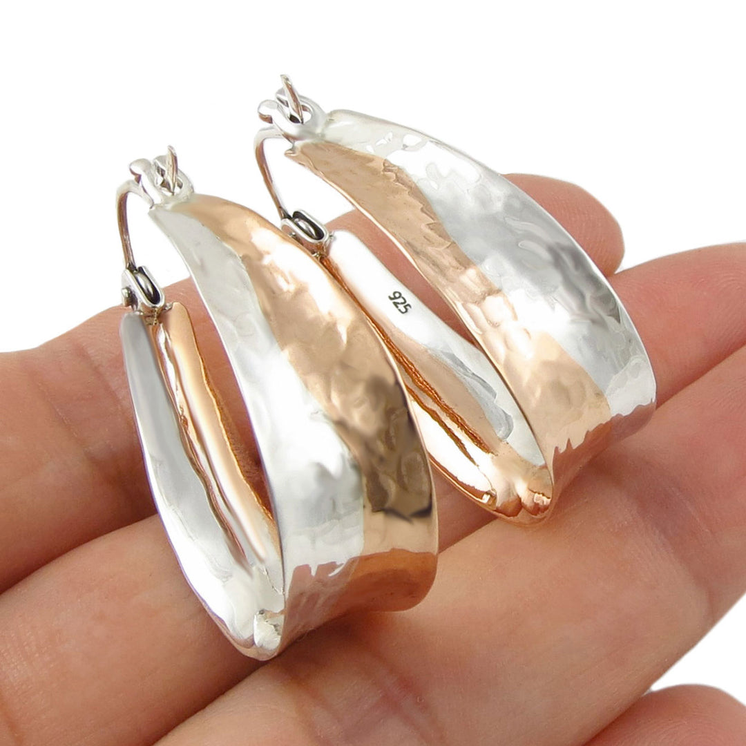 Pair of silver and copper hoop earrings held in a hand against a white background