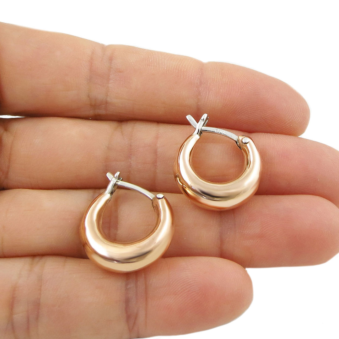 Solid copper and silver two tone small circle hoop earrings held in a person's hand.