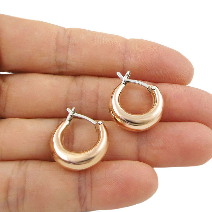 Solid copper and silver two tone small circle hoop earrings held in a person's hand.