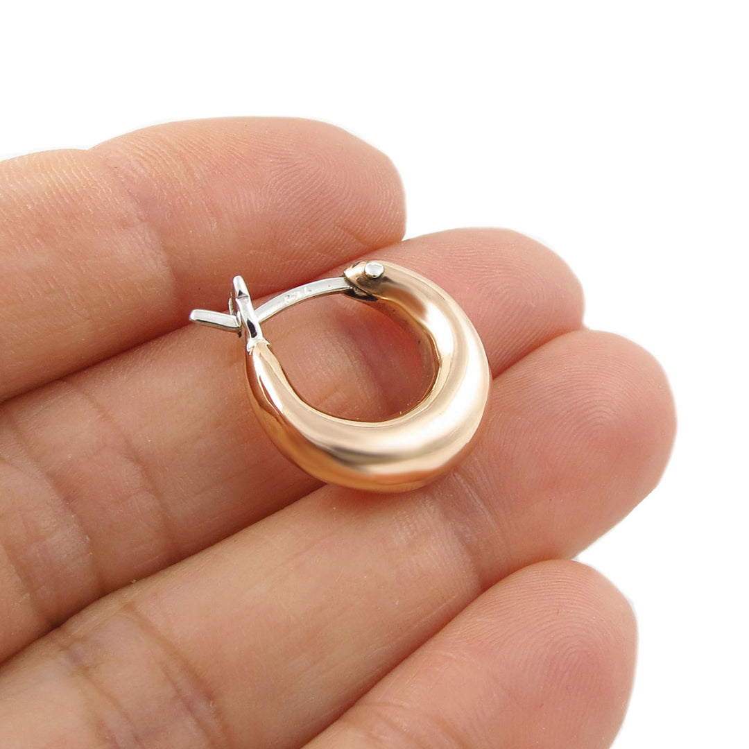 A single copper and silver circle hoop earring held in a person's hand, 