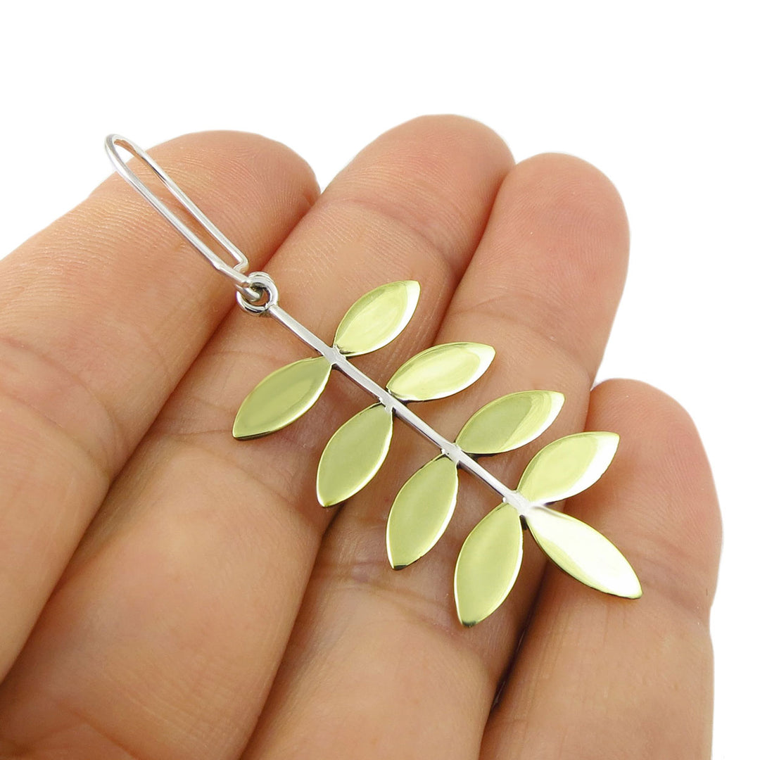 Gold leaf-shaped earring held between fingers on a white background