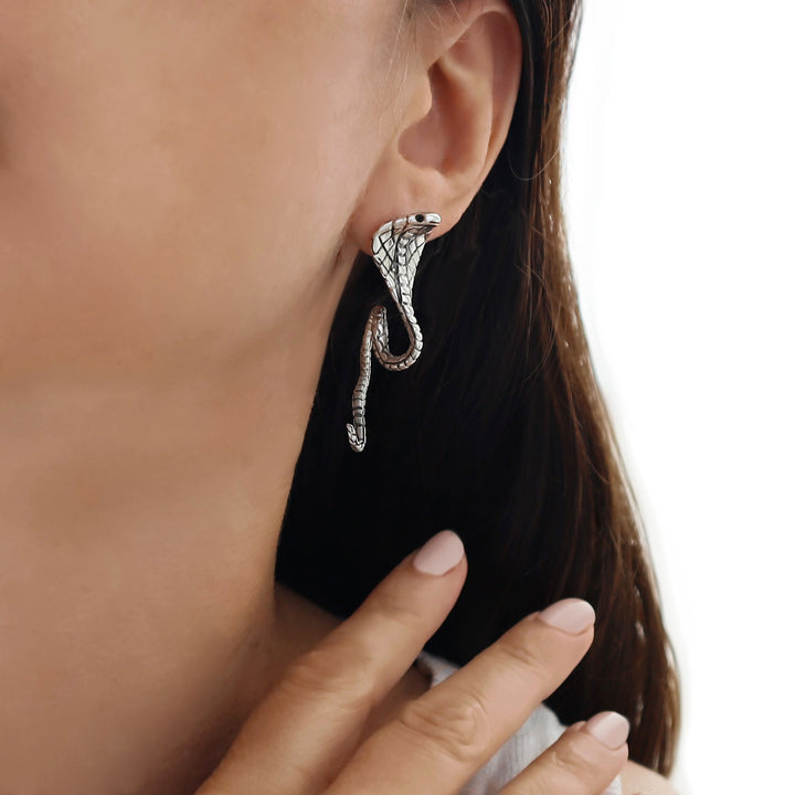 Silver cobra snake-shaped earring worn by a person with a blurred background