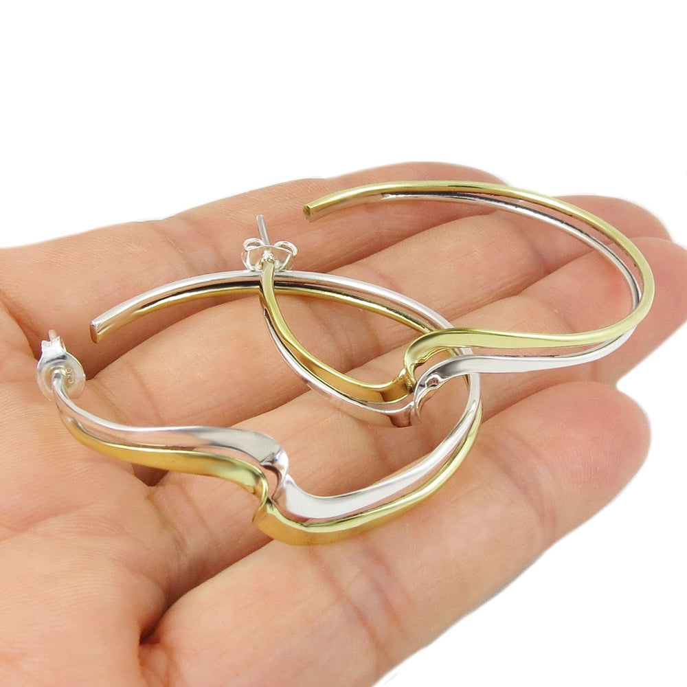 Gold and silver hoop earrings held in a hand against a white background