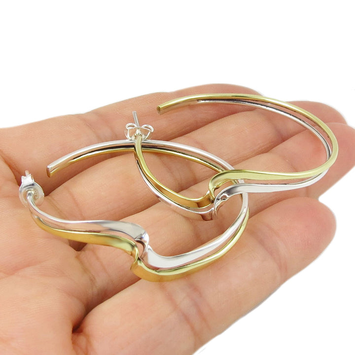 Gold and silver hoop earrings held in a hand against a white background