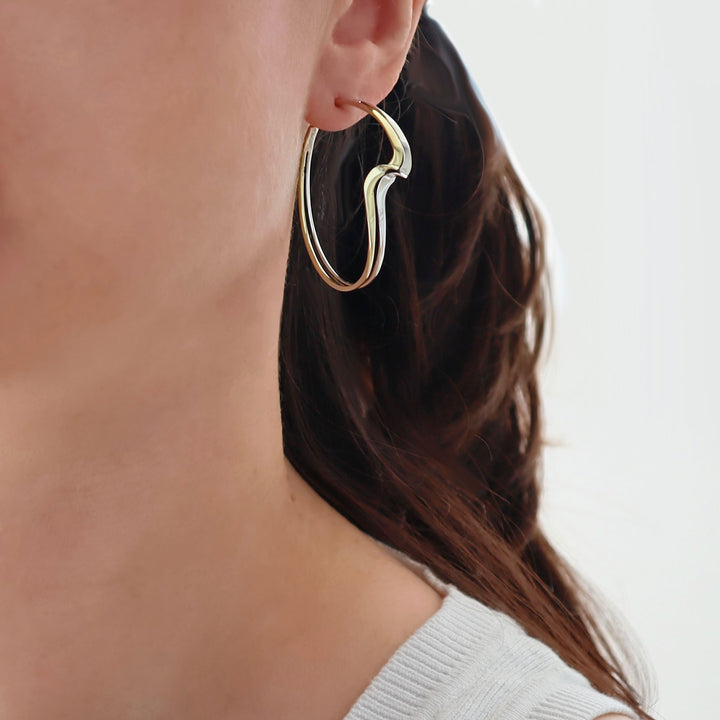 A woman wearing a large curved hoop earring in gold and silver. 