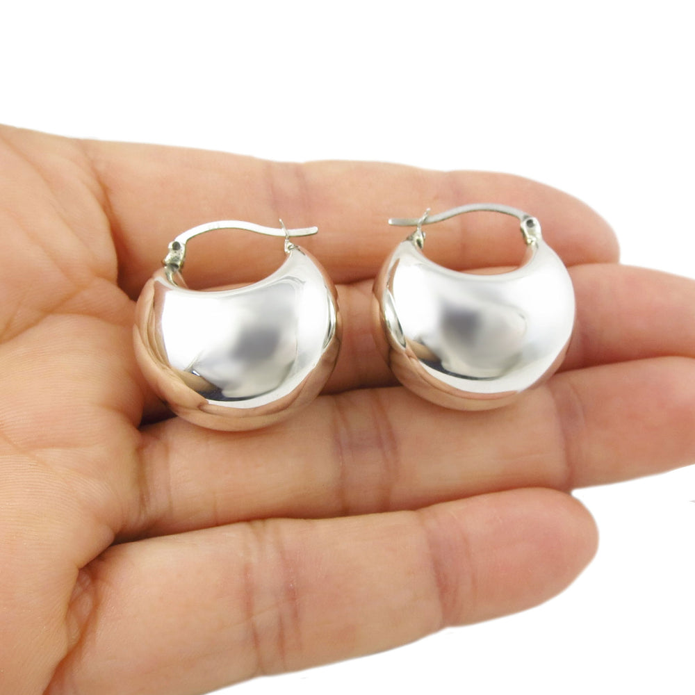 Handmade silver chubby dome hoop earrings held in a hand on a white background