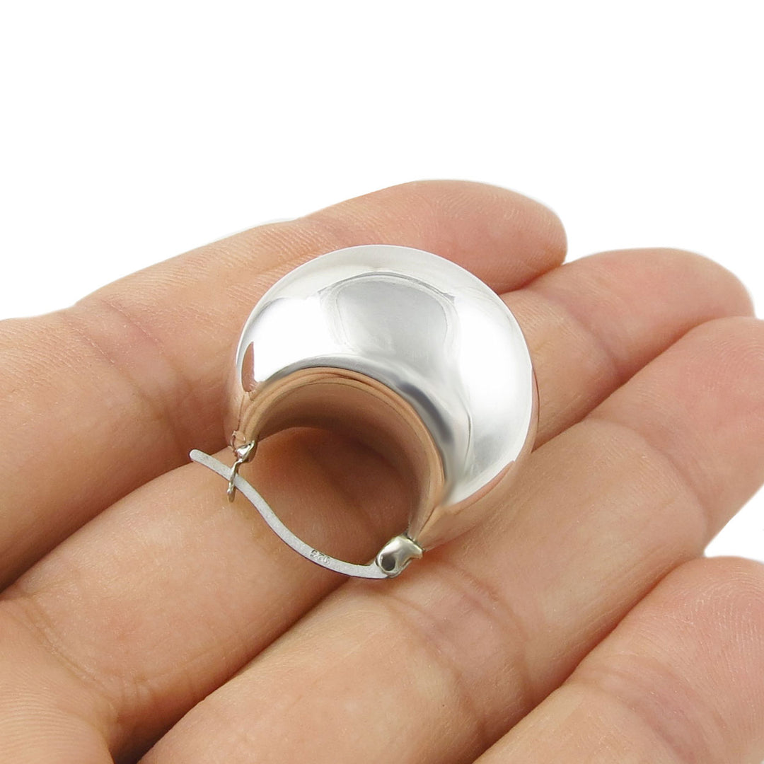 A single handmade sculptural chubby dome hoop silver earring held between fingers on a white background