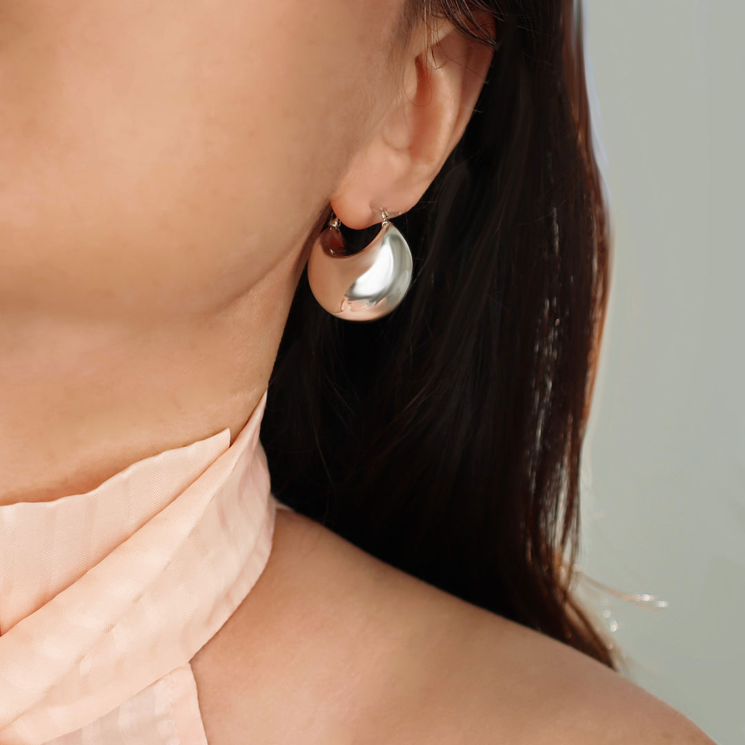 Close-up of a woman wearing a silver chubby dome hoop earrings with a neutral background
