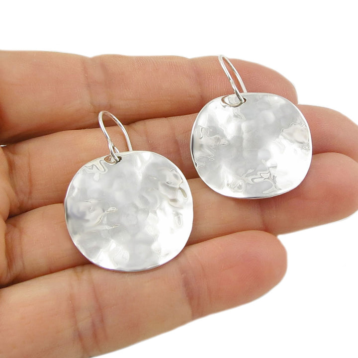 Hammered 925 silver curved round earrings held between fingers on a white background