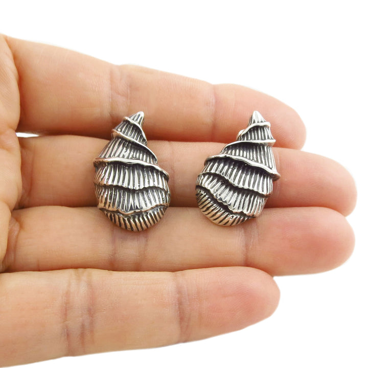 Large Mexican sterling 925 silver mollusc shell earrings held in a person's hand on a white backgroud. 