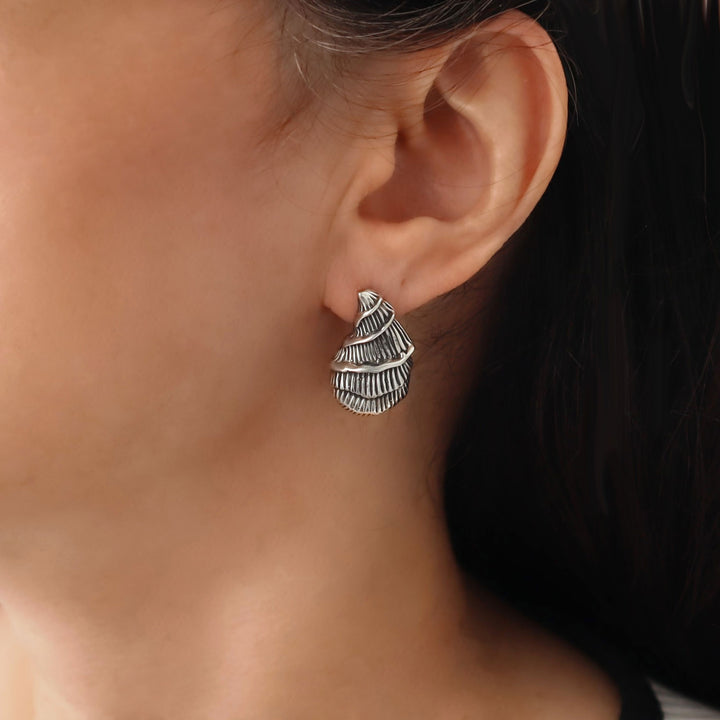 Large handmade seashell earring in polished and antiqued 925 sterling silver worn by a woman with dark hair
