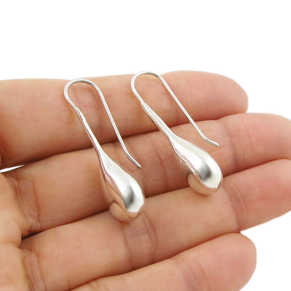Long handmade ladies sterling 925 silver polished teardrop earrings held in a persons hand. 