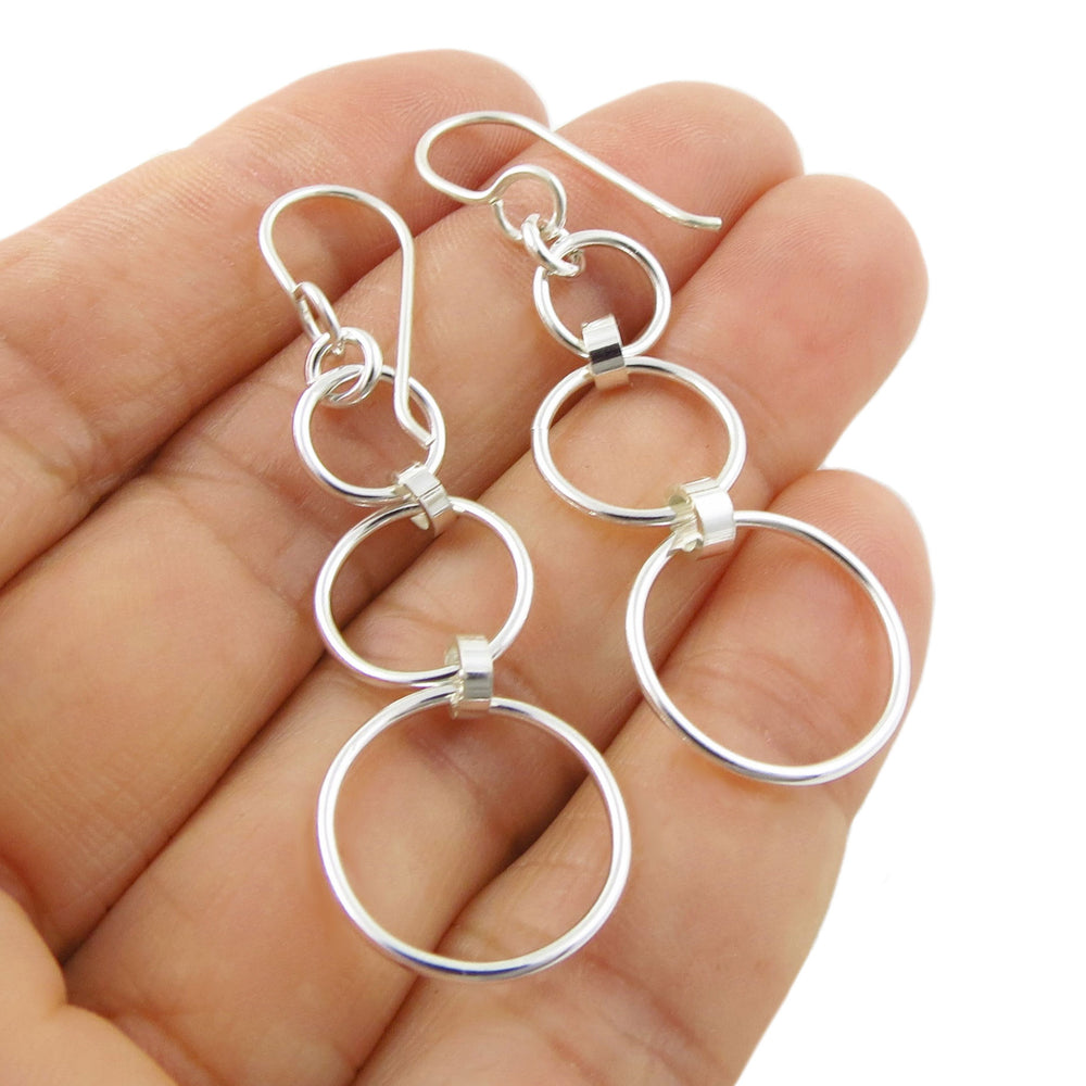 Long solid 925 silver hoop earrings held between fingers on a white background