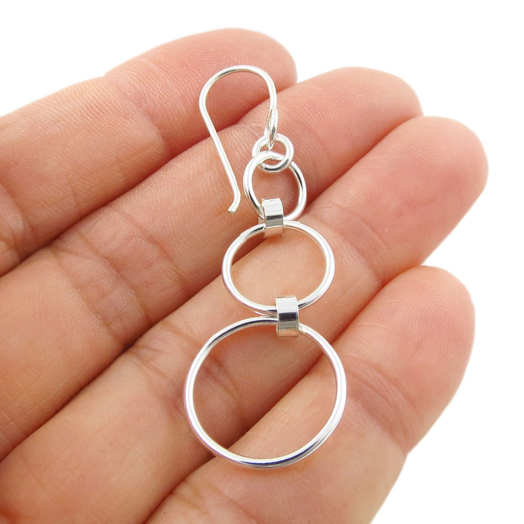 Long 925 silver hoop earring featuring three circles held between fingers on a white background