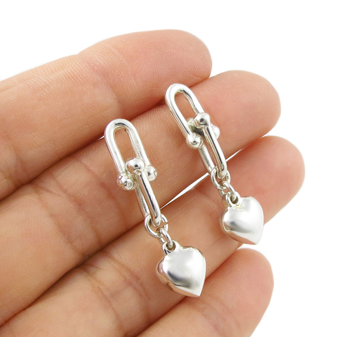 Gauge link and 925 ssilver heart-shaped earrings held between fingers on a white background
