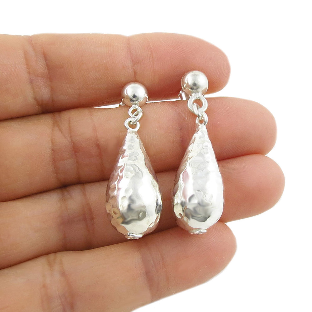 Heavy raindrop hammered sterling silver dangle earrings held in a person's hand