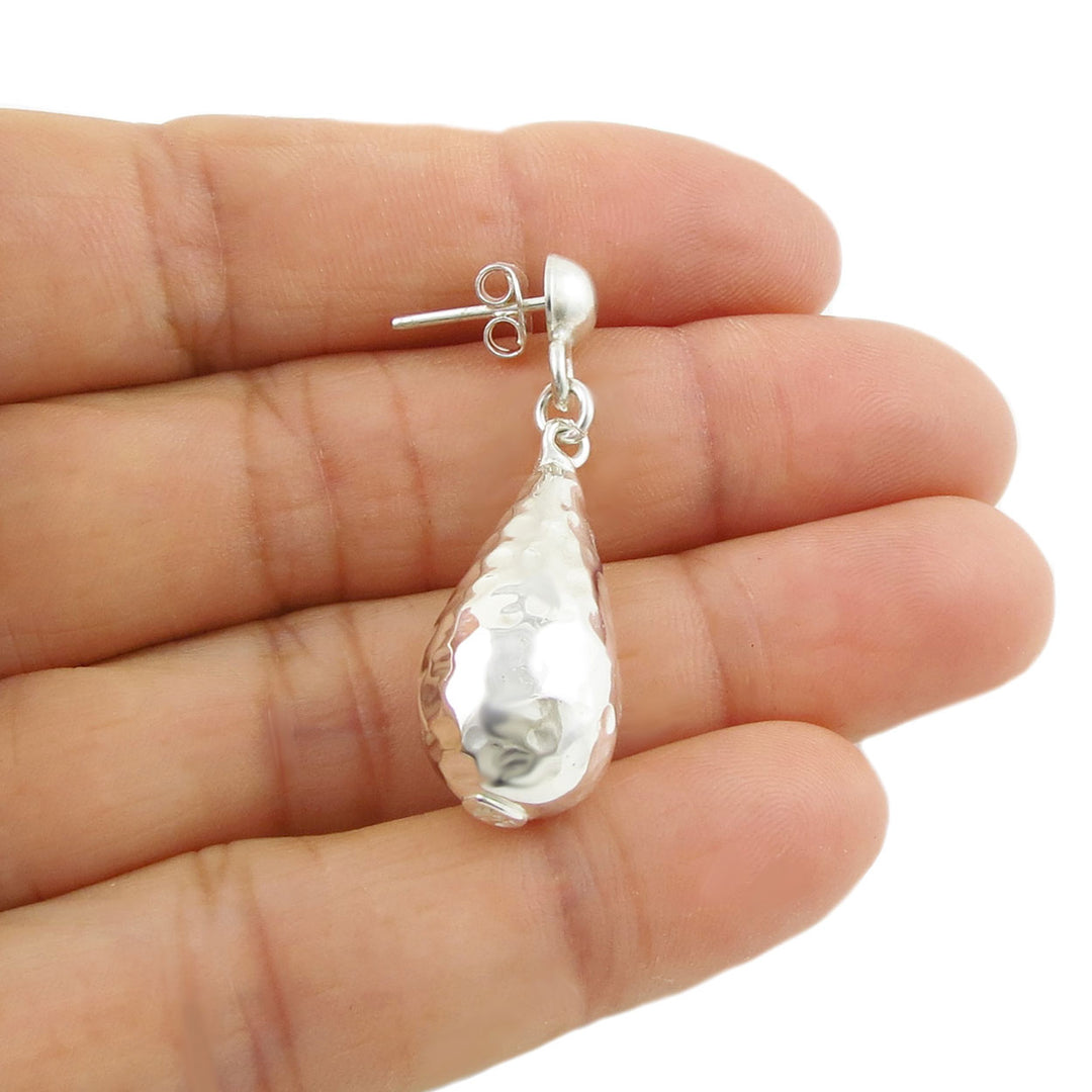 A single puffed 925 sterling silver hammered raindrop earring held in a person's hand 
