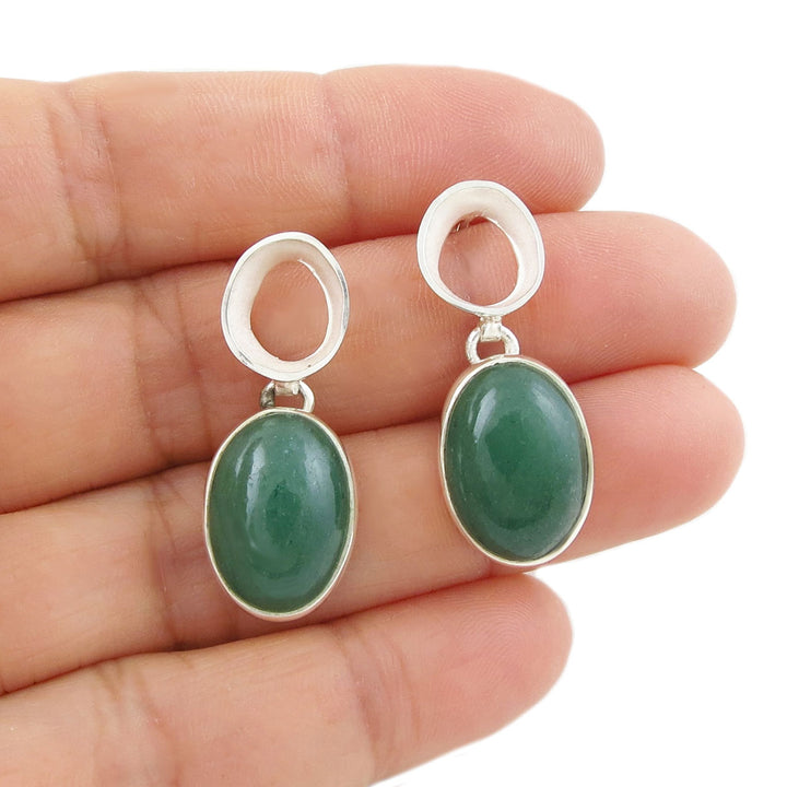 A large pair of Mexican design handmade sterling 925 silver drop earrings with green aventurine gemstones held in a peron's hand.
