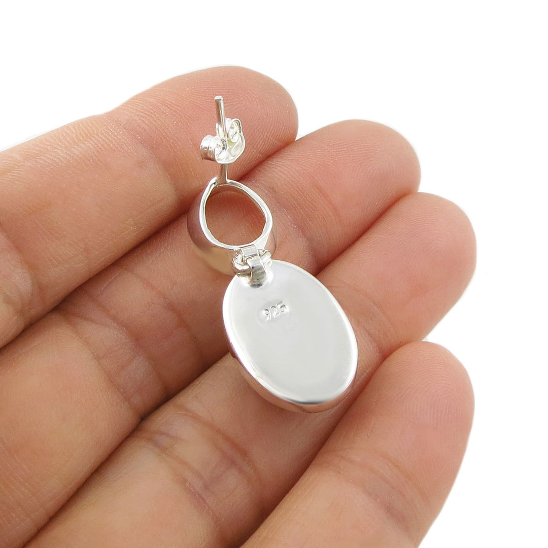A silver earrings held upside down in a person's hand showing the stamp 925. 