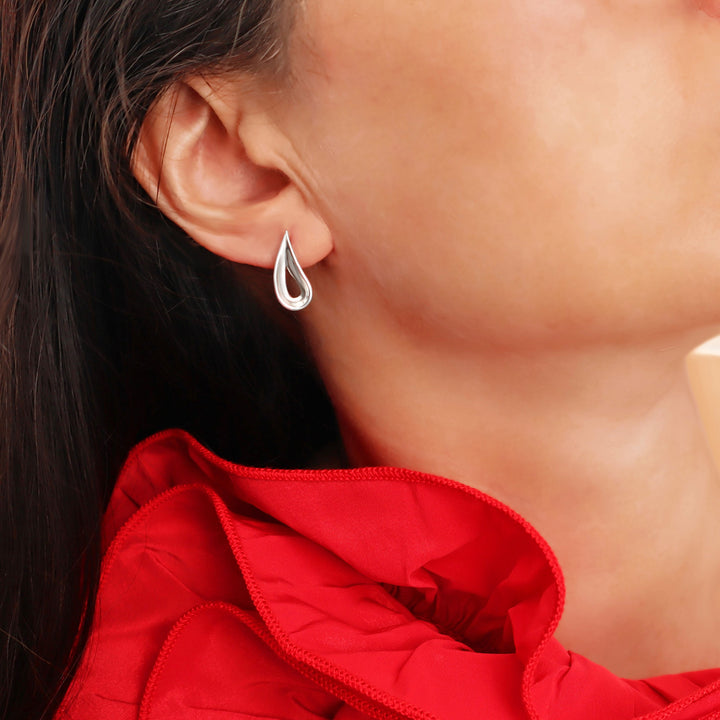 Close-up of a woman wearing a 925 sterling silver teardrop earring with a curved edge and a red dress in the background.