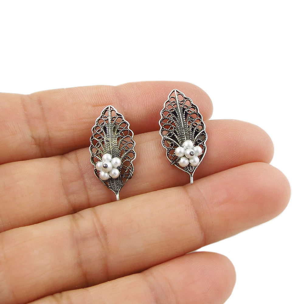 A pair of stud earrings in the shape of leaves in 925 sterling silver with ornate filigree work and seed pearls