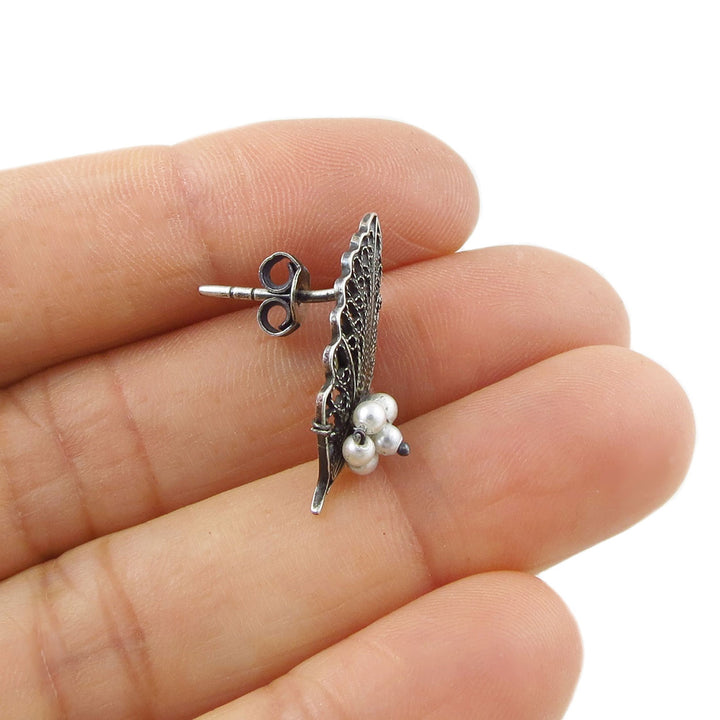 A single earring in the shape of a leaf in 925 silver with pearl acents held in a person's hand