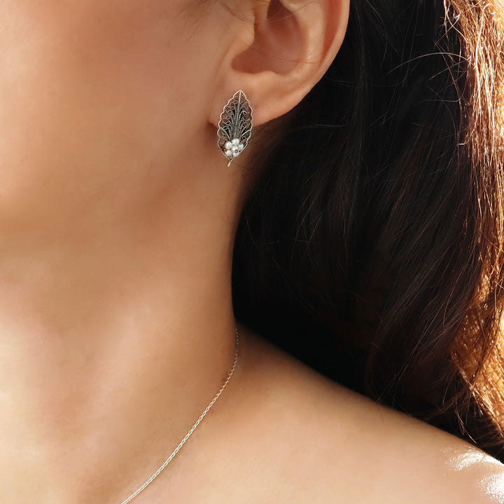 Woman with dark hair wearing a statement leaf shaped sterling silver stud earring decorated with seed pearls