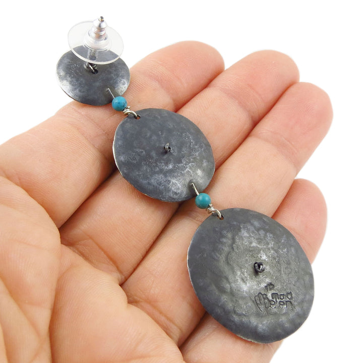 Hand holding a single 925 sterling silver disc earring showing the maker's mark of Maria Belen Nilson