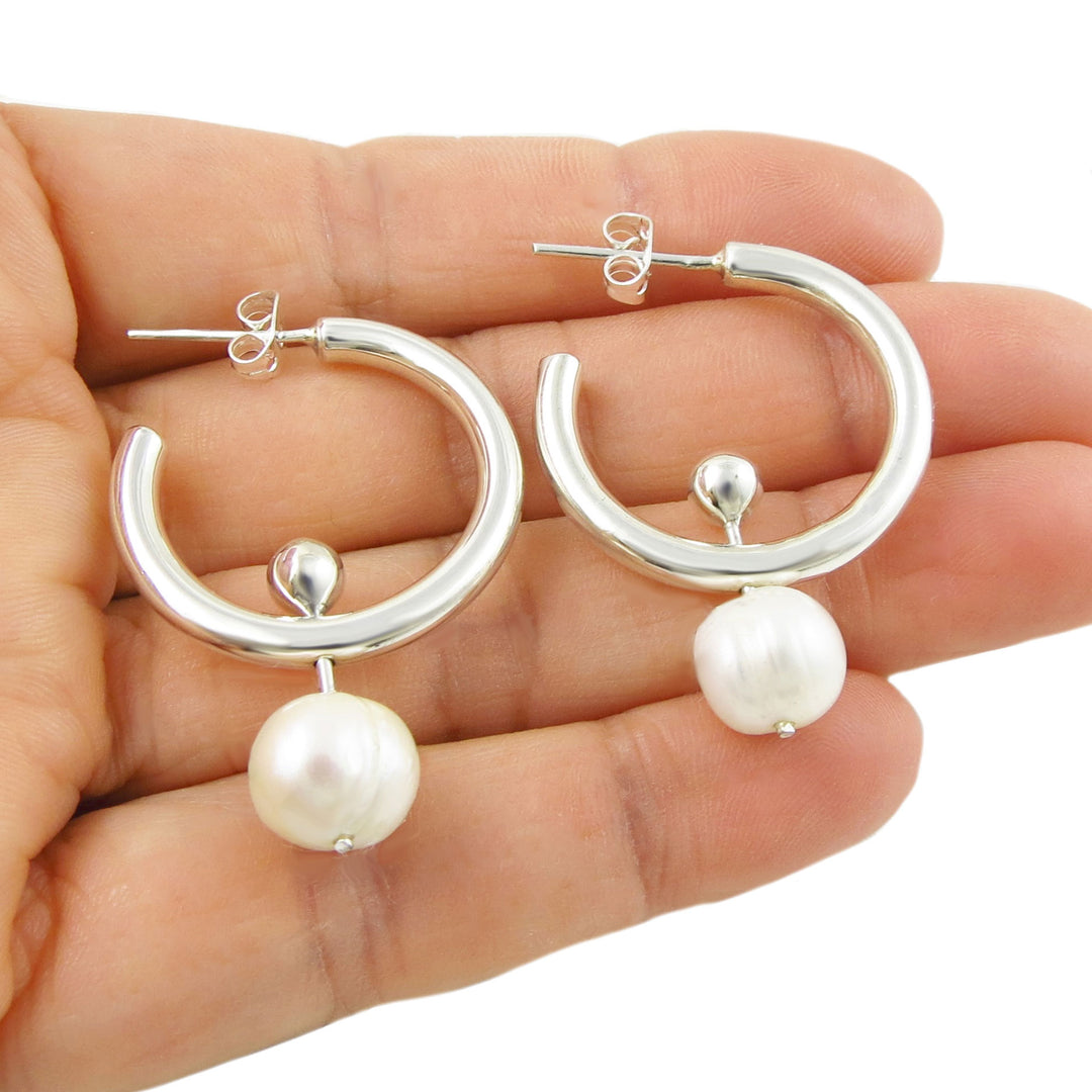 Large 925 sterling silver modern hoop earrings with pearls drops held in a hand on a white background