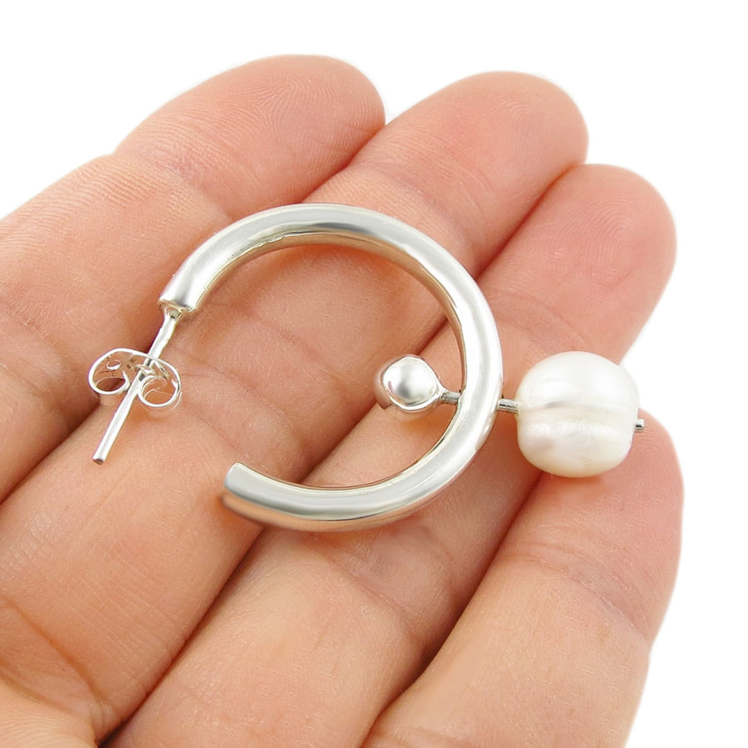 Polished 925 sterling silver hoop earring with a pierced pearl held in a hand on a white background