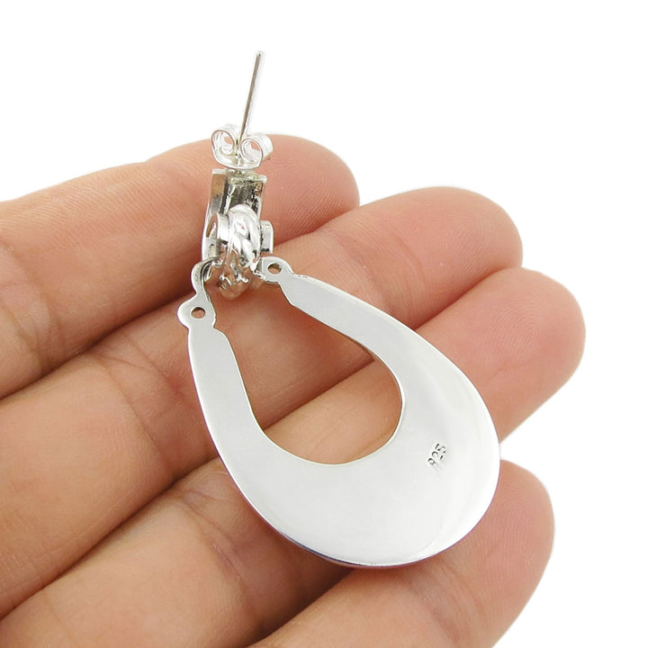 A large sterling silver hoop earring with a butterfly and post held upside down in a person's hand to show the 925 hallmark.