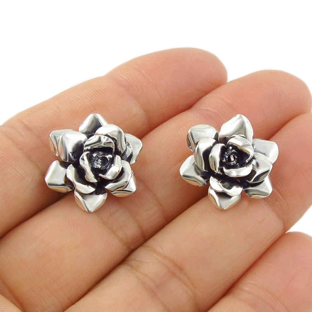 Handmade jewellery UK 925 Silver rose flower-shaped earrings held between fingers on a white background