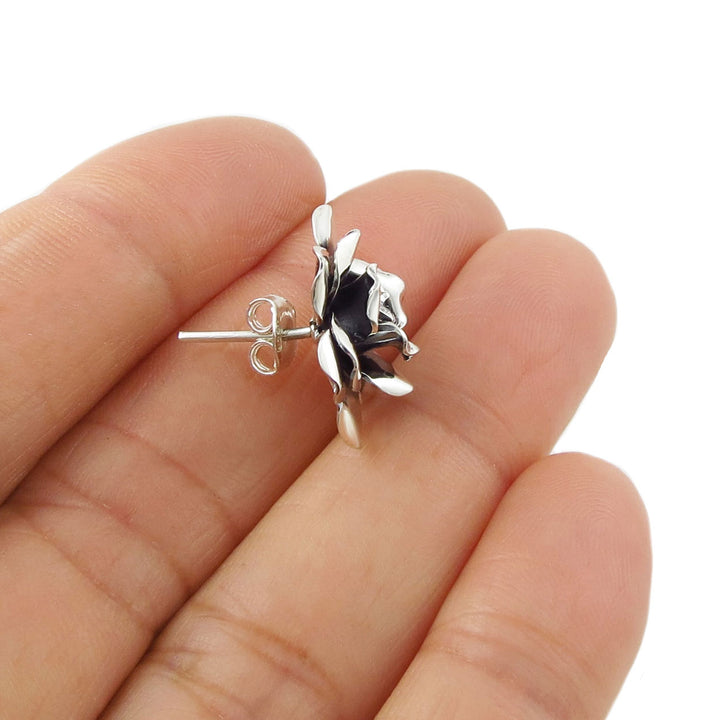 A single silver rosse flower-shaped earring held between fingers on a white background