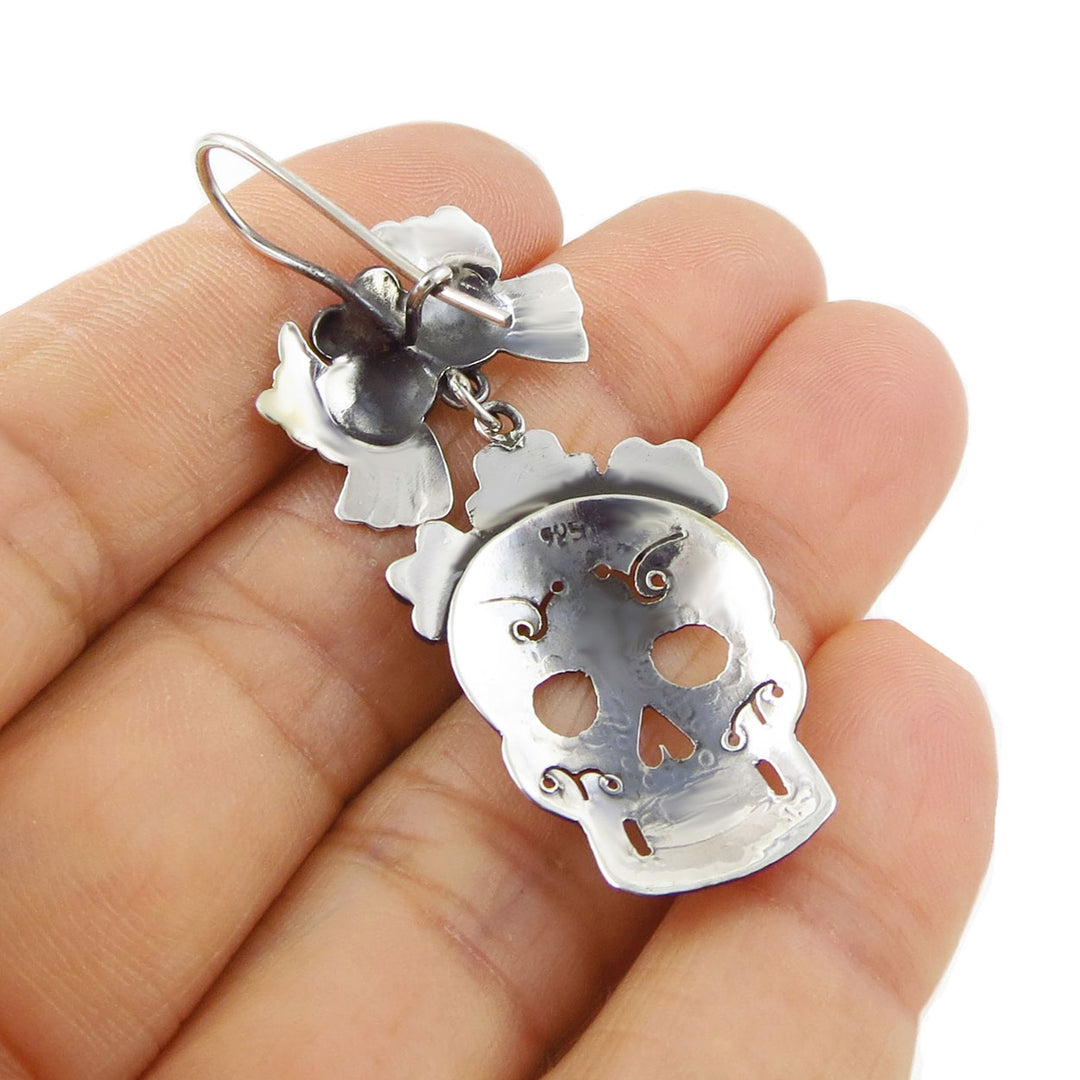 Mexican day of the dead sugar skull-shaped 925 sterling silver earring held upside down in a hand against a white background. 