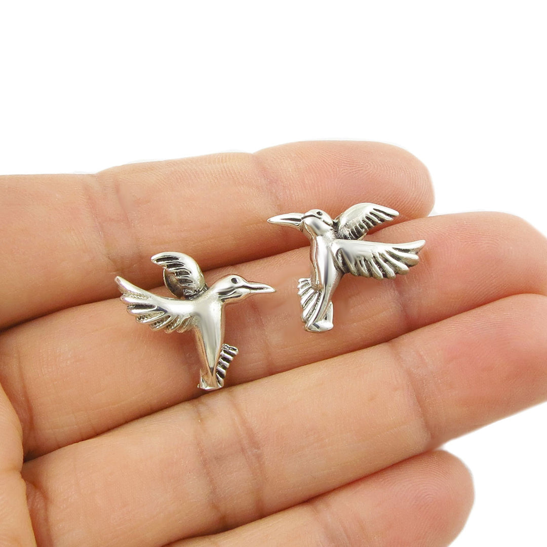 Mexican 925 sterling silver bird stud earrings held between fingers on a white background